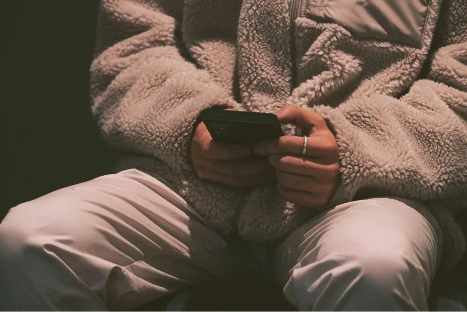 Person in a soft fleece jacket holding a smartphone, evoking emotional withdrawal and digital detachment.