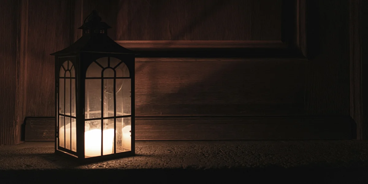 A lit lantern casting a soft light in a dark wooden interior, suggesting guidance in uncertainty.