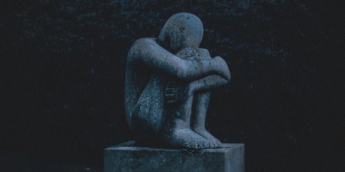 stone sculpture of a bent-over human figure in low light.