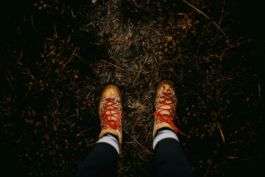 A person standing still on straw-covered ground, wearing boots.