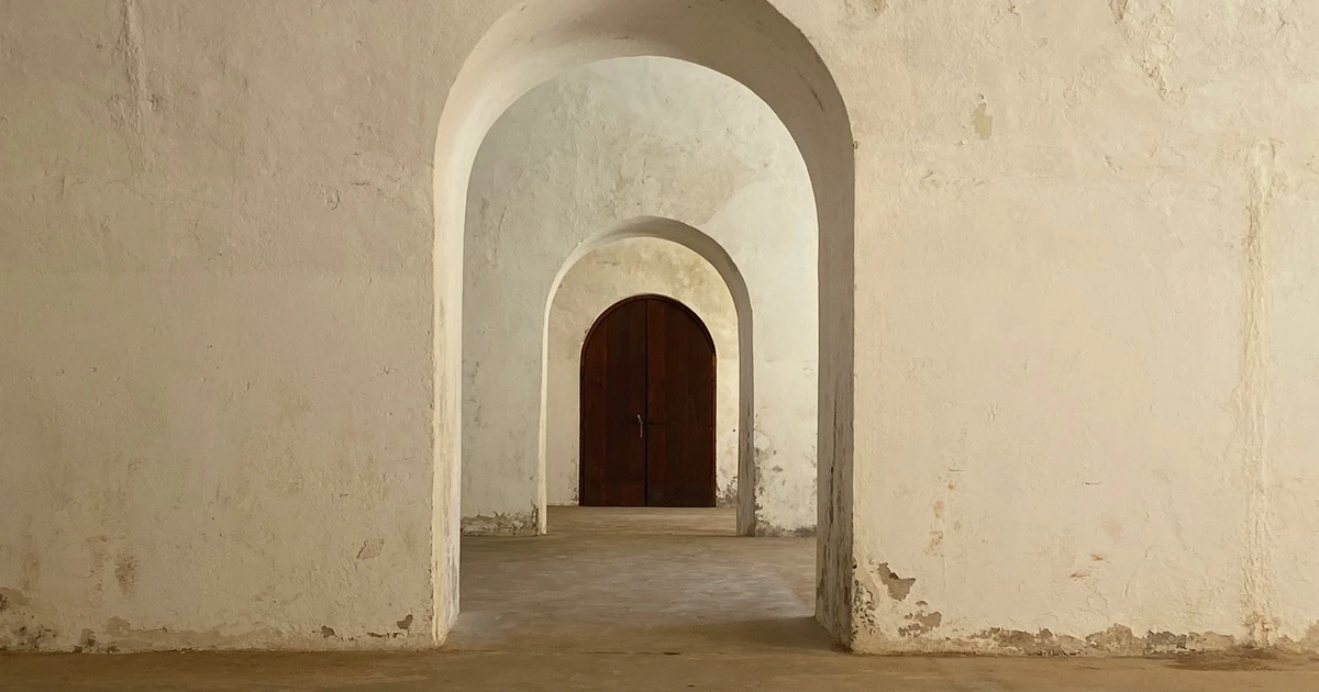 A series of arched stone doorways leading to a closed wooden door, lit by soft natural light.