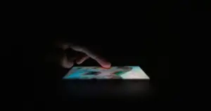 Finger interacting with a smartphone screen in darkness, representing digital interaction and social media use.