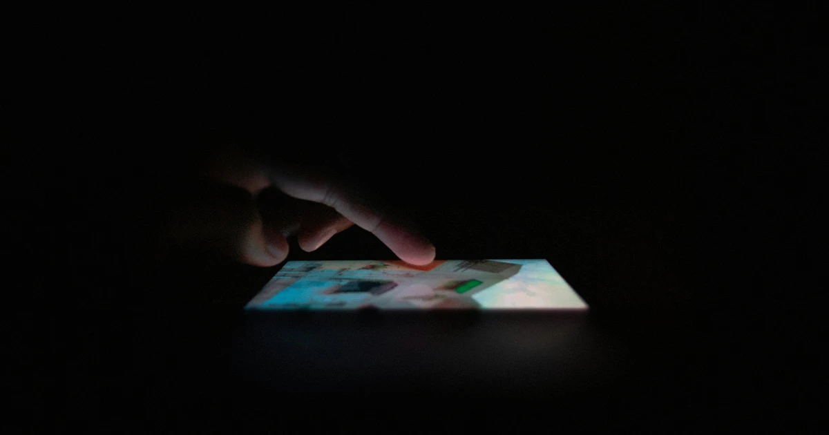 Finger interacting with a smartphone screen in darkness, representing digital interaction and social media use.